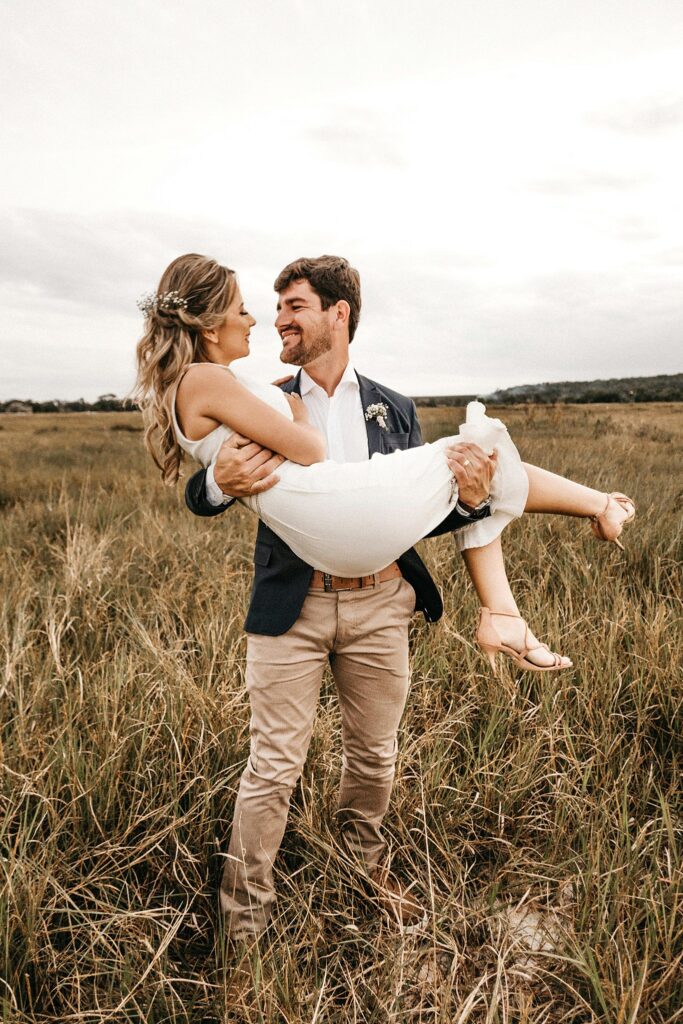 Engaged couple in a field of tall grass with man holding woman.