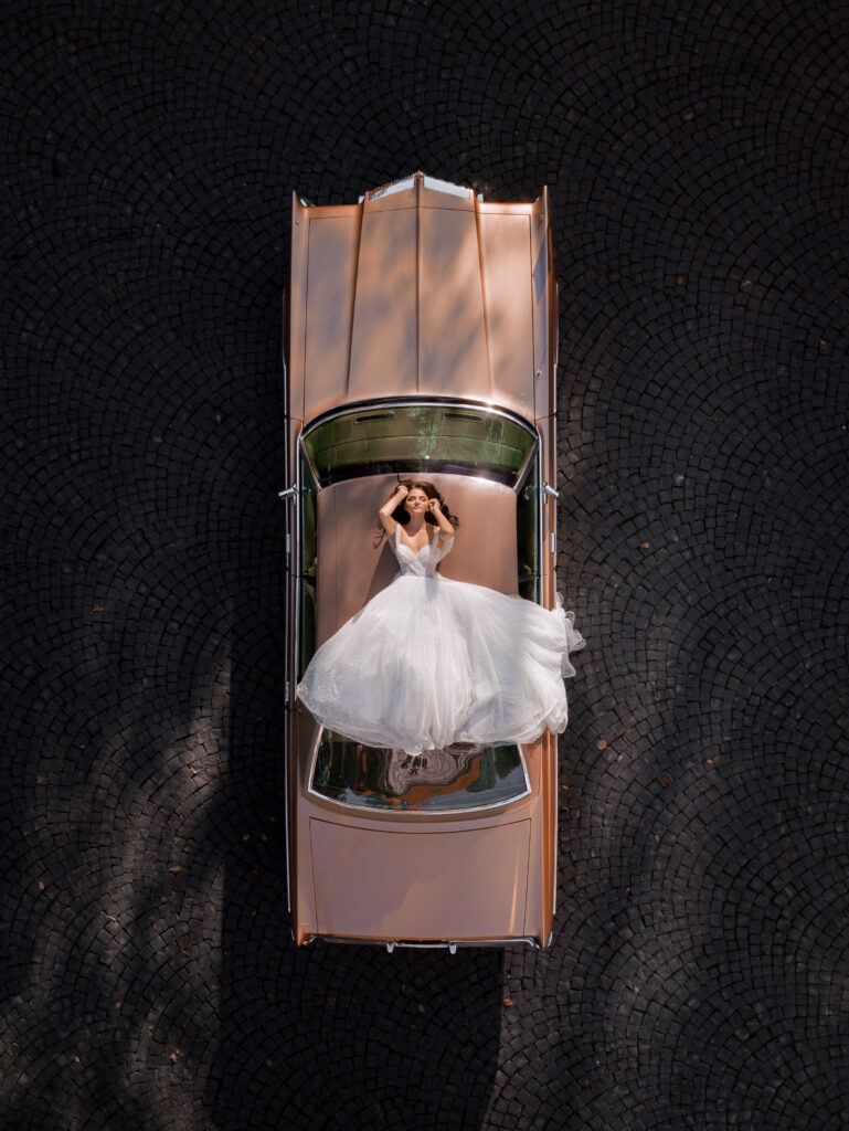 Aerial view of elegant bride lying on the roof of a pink retro car. Concept of bride