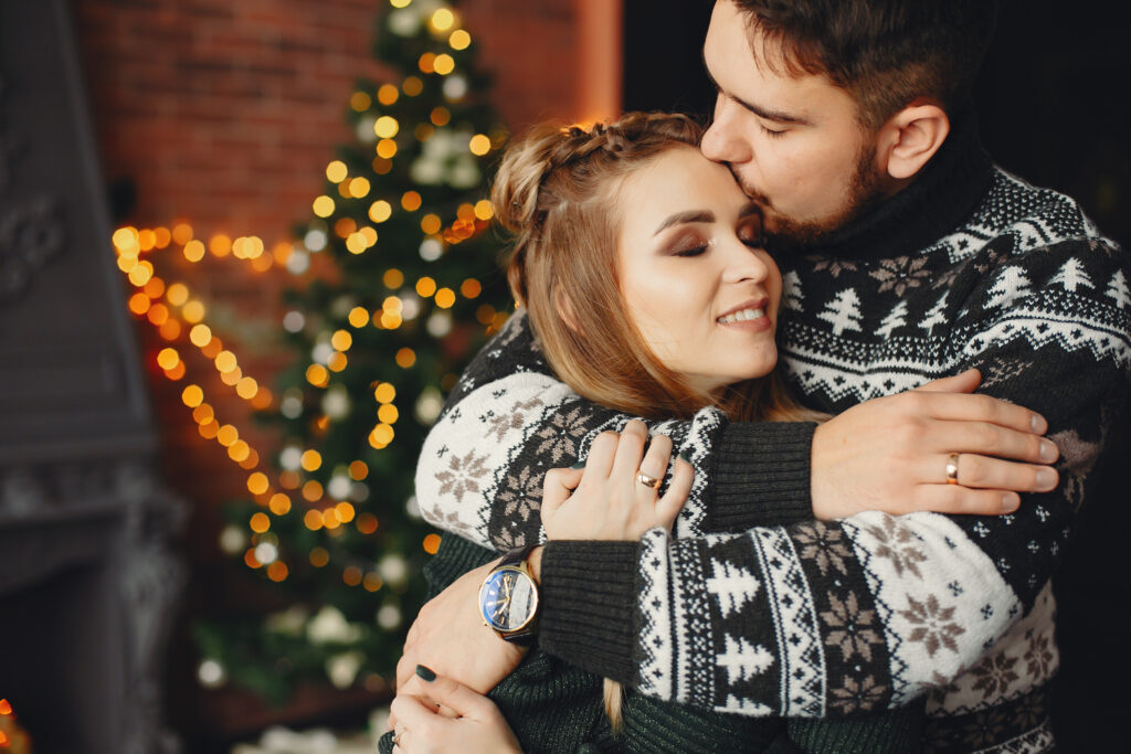 couple in christmas sweaters hugging during engagement session