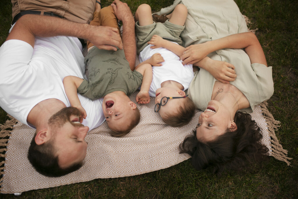 family laying down on blanket laughing and tickling each other.