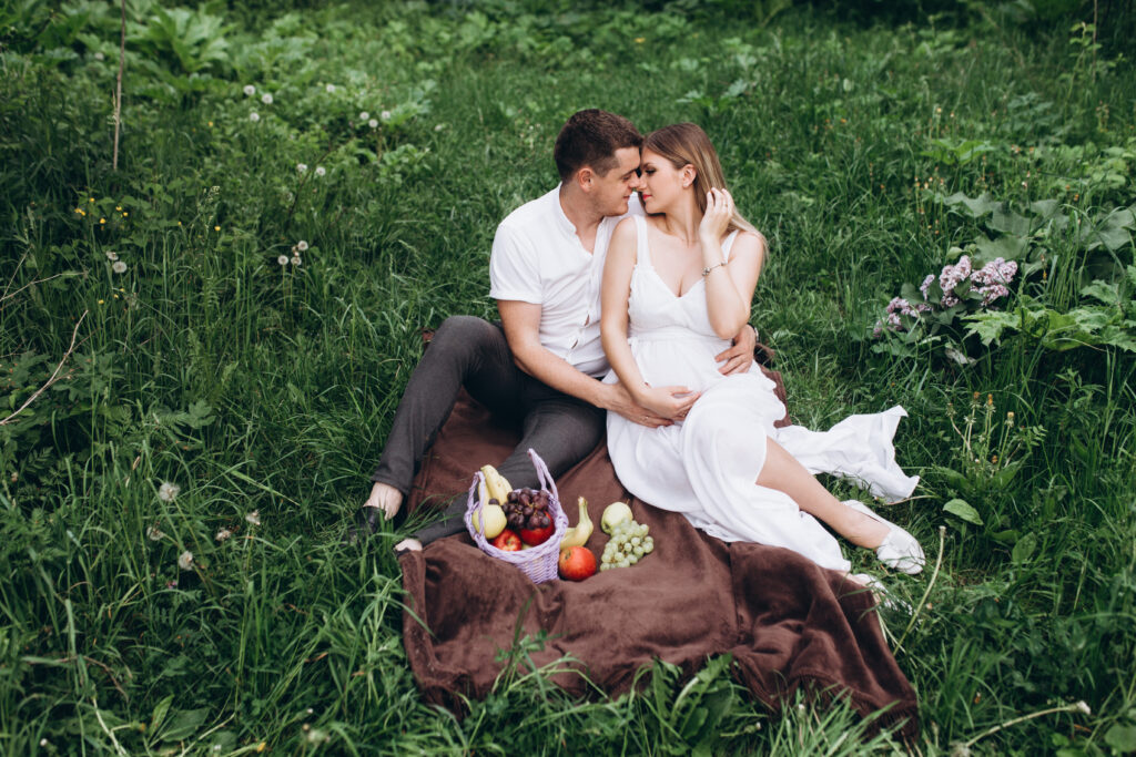 The wife and husband sitting on the plaid with fruits.